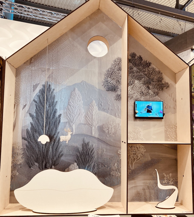 Tapentenpräsentation, kleines Modellhaus im Querschnitt mit angedeuteten Zimmern, 2 Lampen, 1 Fernseher, ein Sofa, 1 Stuhl, Tapetenmotiv: pastellfarbener Wald mit Hirsch