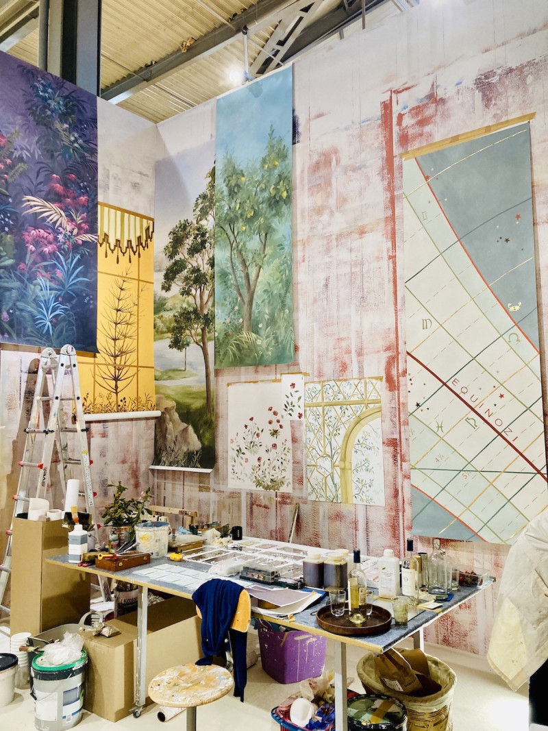 Messestand mit Ateliercharakter, viele verschiedene Malutensielien, Tapetenbahnen mit verschiedenen gemalten oder bedruckten Motiven