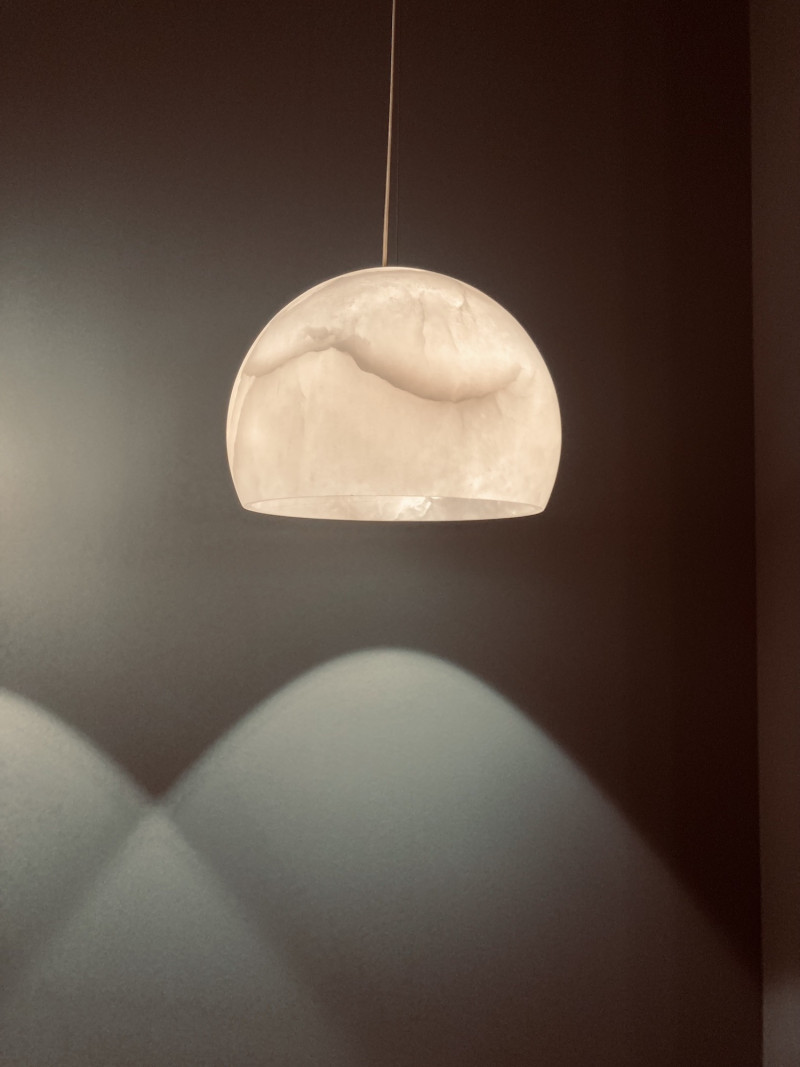 Pendelleuchte aus hellem Marmor mit typischer Maserung vor graphitfarbener Wand, Licht- und Schattenspiel