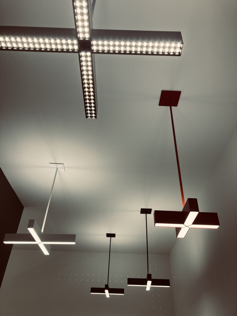 5 Lampen in Kreuzform, an Metallstangen von der Decke hängend, Farbe 2 x schwarz, 2 x Aluminium, 1 x rot, Licht an 4 Kreuzen einfaches Weiß, an einem Kreuz s/w gerastertes Licht