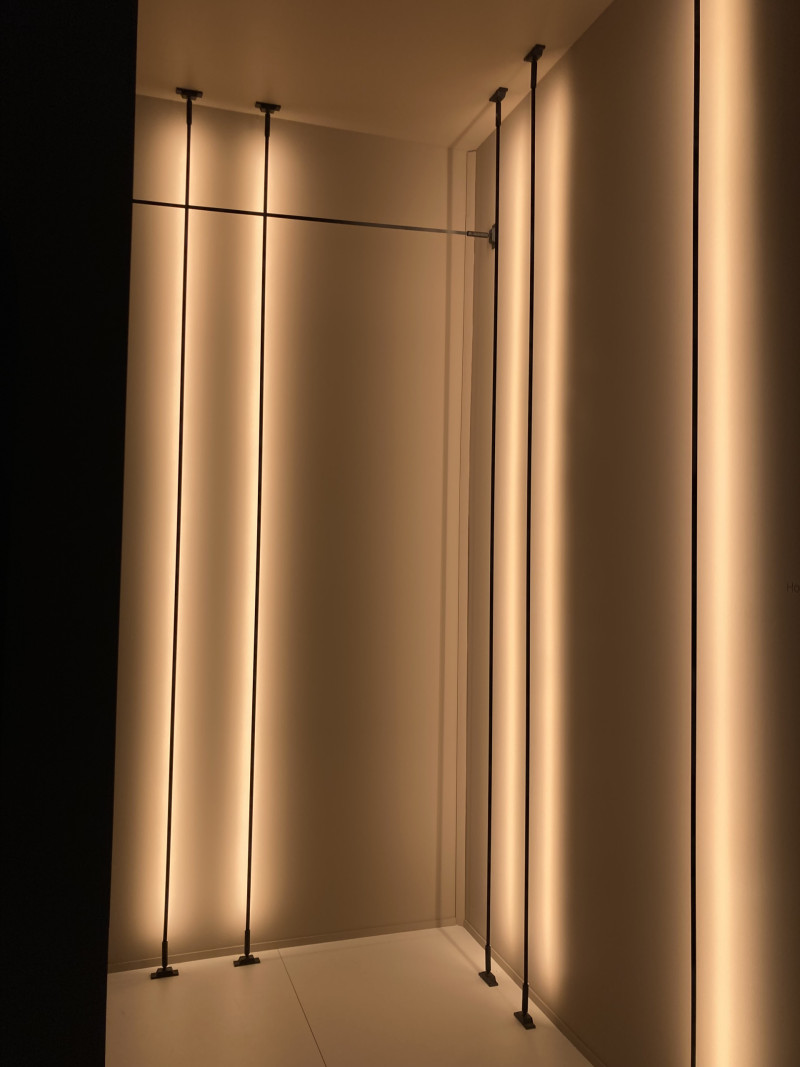 Wandleuchten in Form von Metallschienen, die eingespannt werden zwischen Zimmerdecke und Fußboden. Die Schienen sind mit einem LED-Band bestückt, diese werfen Licht an die Wand, es entsteht ein Schattenspiel