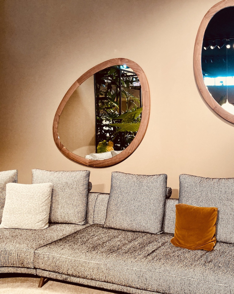 braun/grau melliertes Sofa mit Kissen in verschiedenen Größen, vor einer zimtfarbenen Wand mit 2 organisch geformten, annähernd oval geformten Spiegeln in Holzrahmen